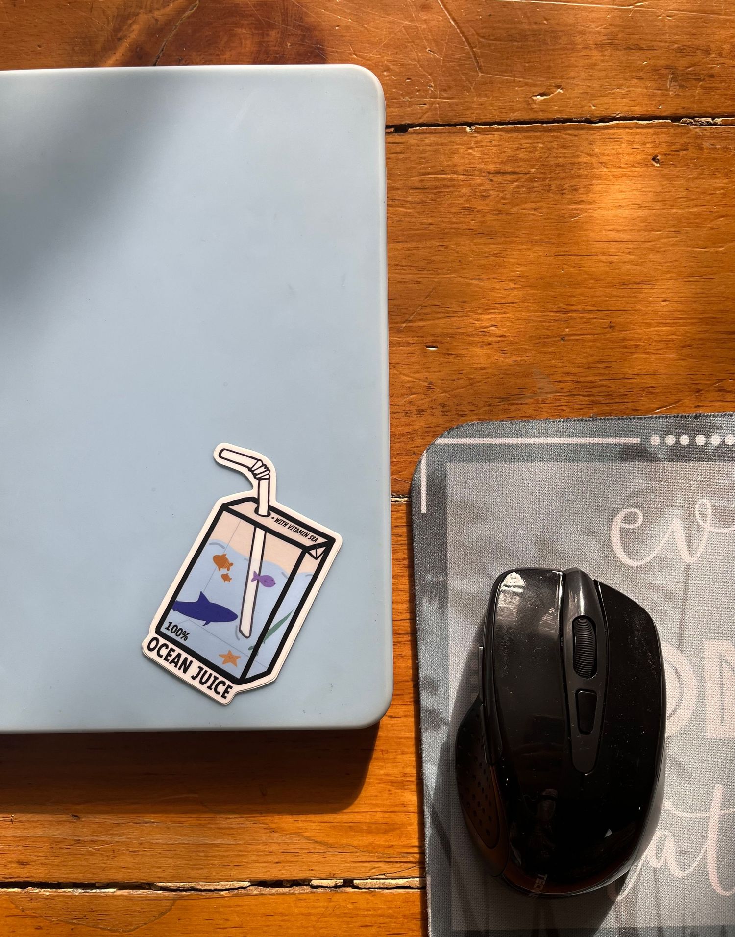 Laptop with decorative stickers displayed on wooden desk surface next to mouse.