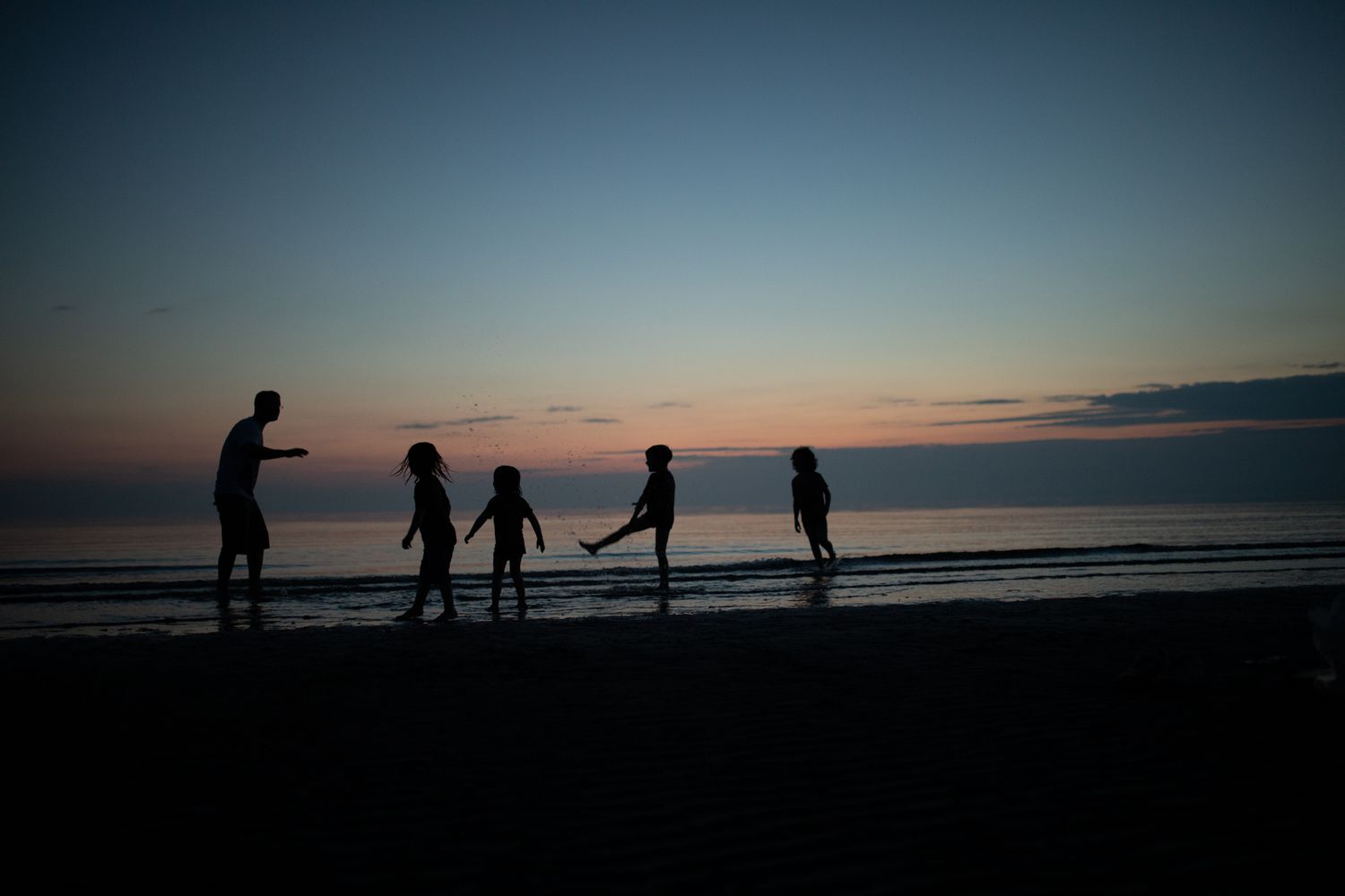 sillohettes of 4 children & an adult playing at the waters edge during blue hour