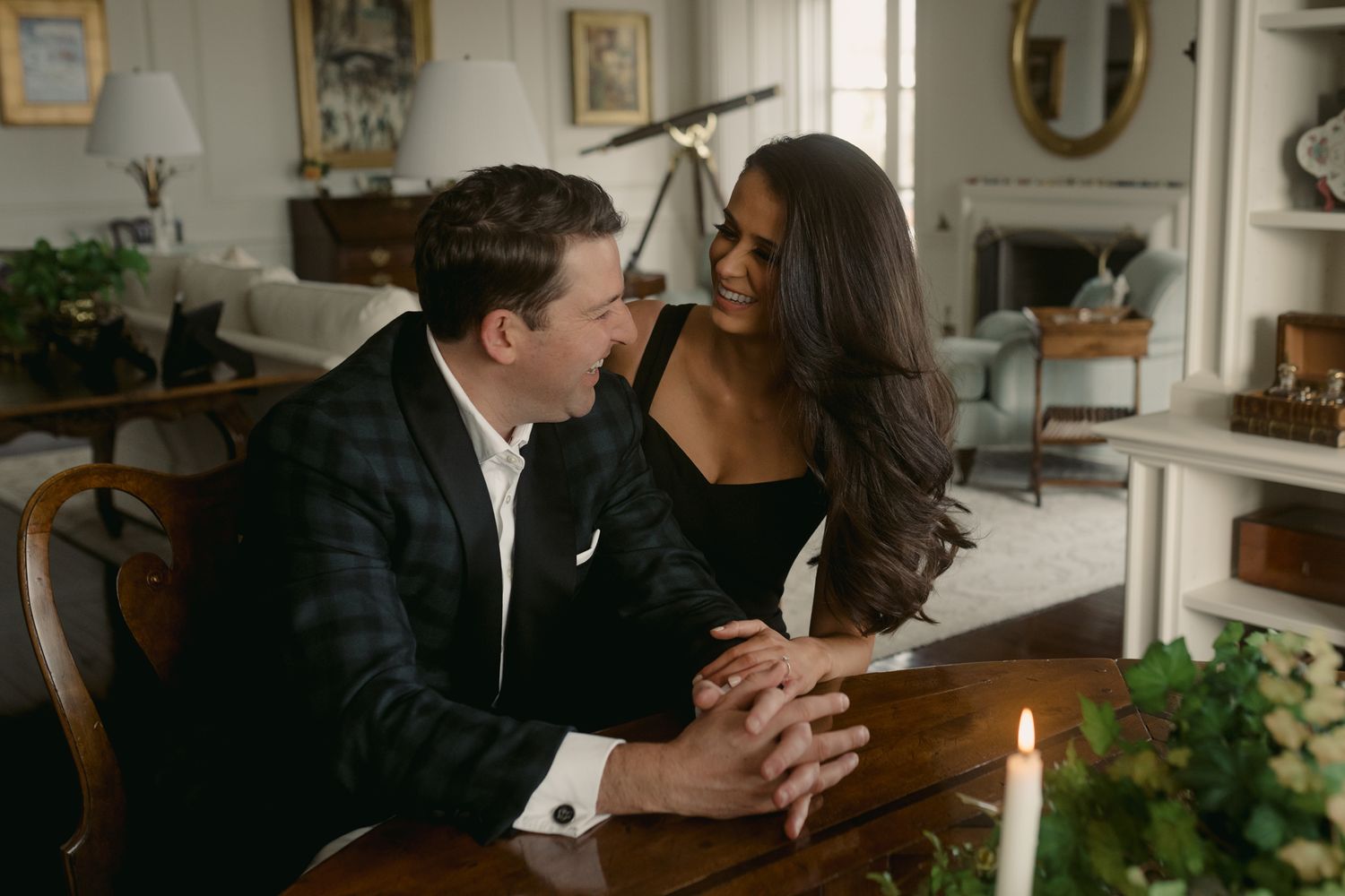 Intimate moment between couple at dinner table with romantic candlelight and greenery decor.