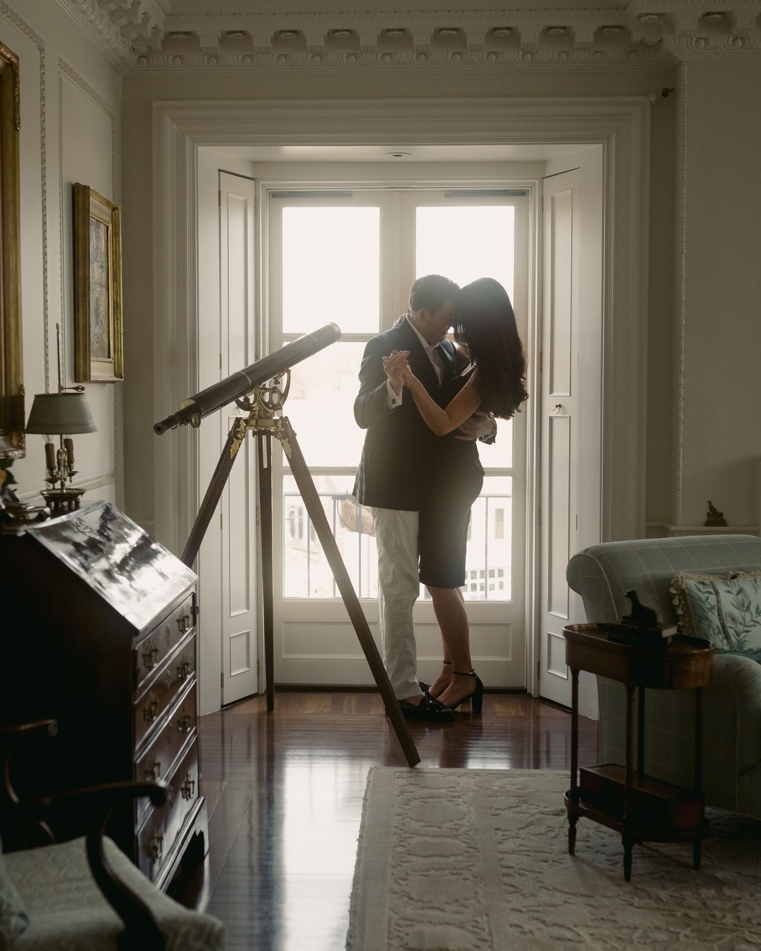 Couple in silhouette dancing in elegant white room with telescope.