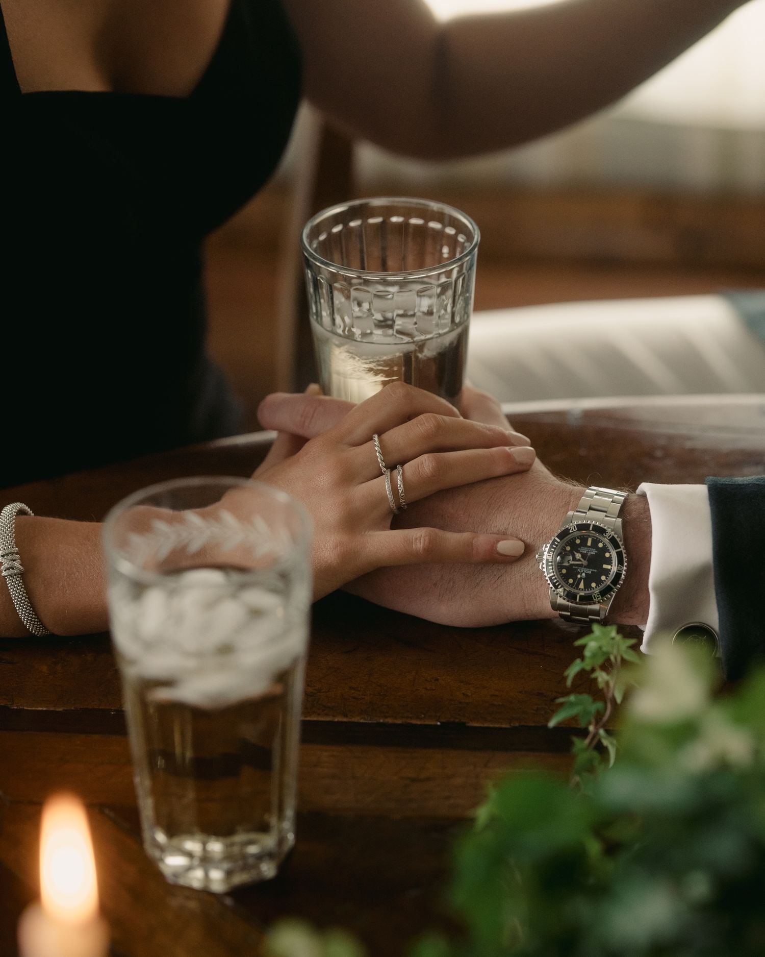 Hands with rings touching across wooden table with drinks.