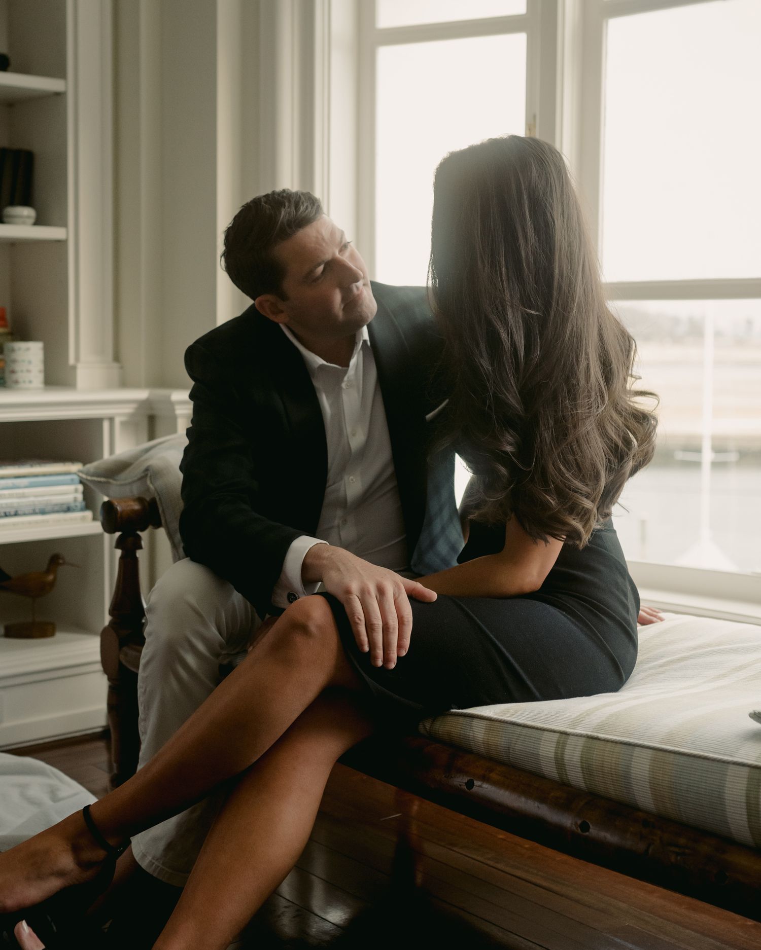 Romantic couple embracing by window in sunlit room.