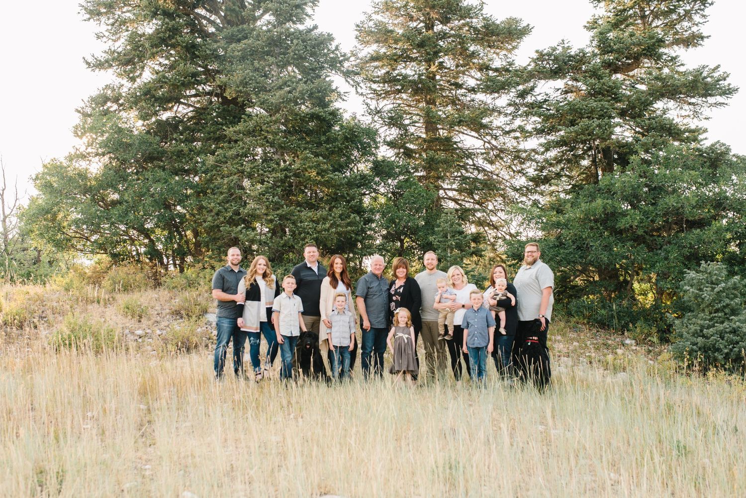 Family group photo in tall grass with evergreen trees in background.