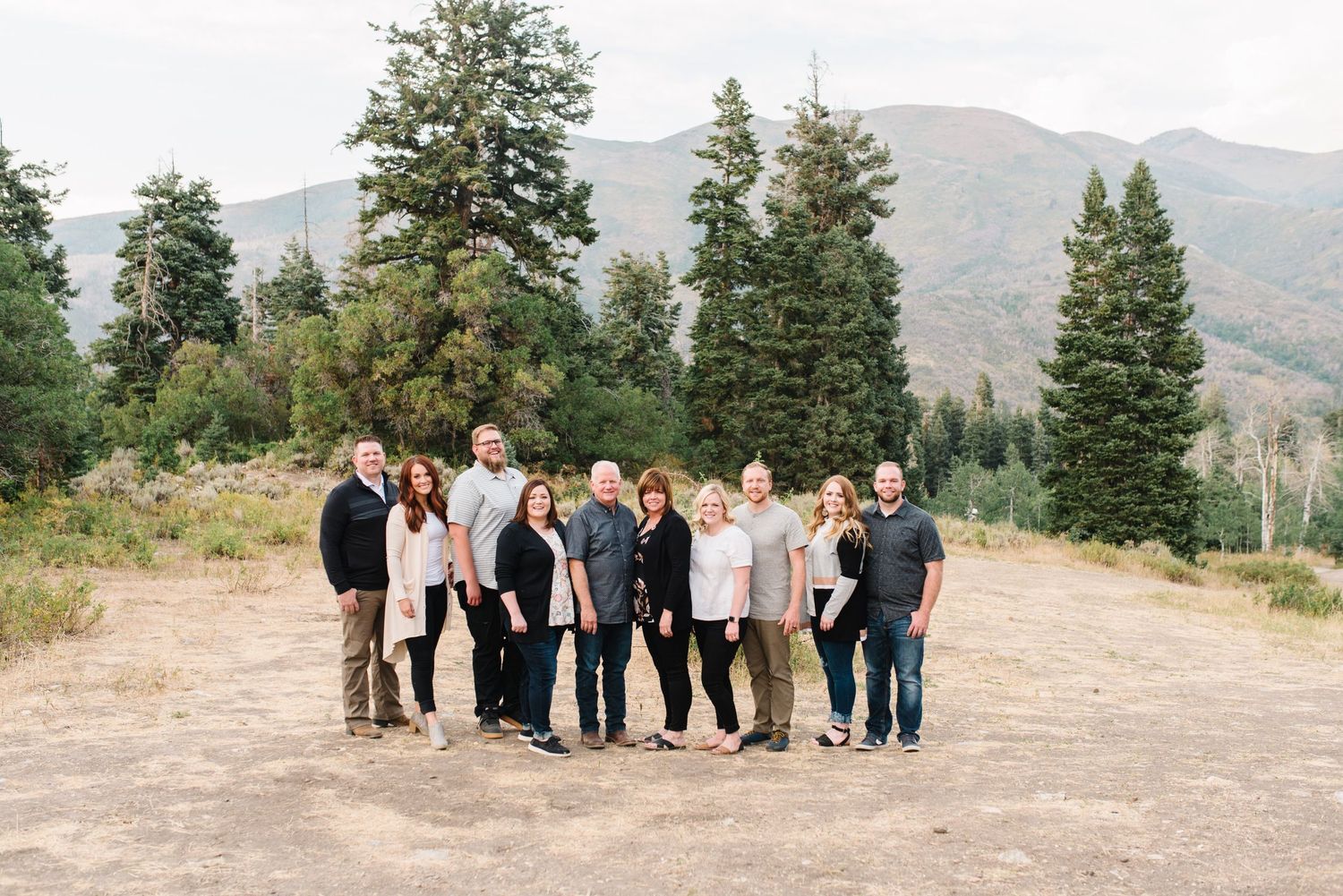 Family gathering posed together on mountain clearing with forest backdrop.