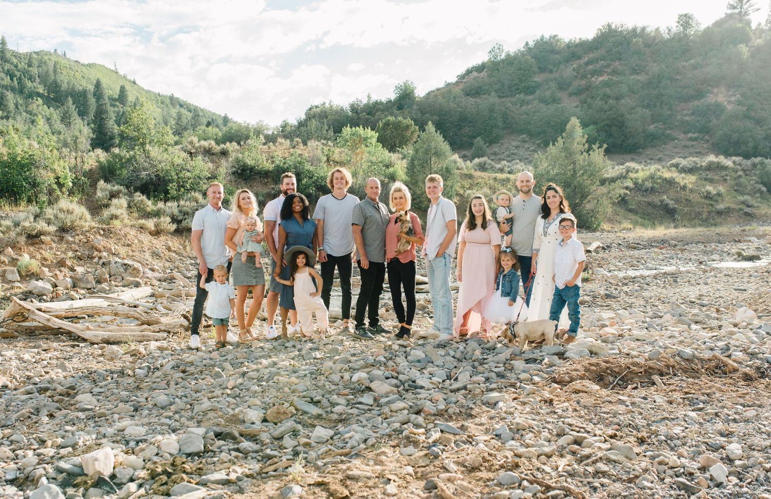 Extended family gathered on rocky terrain with mountains and forest in background.