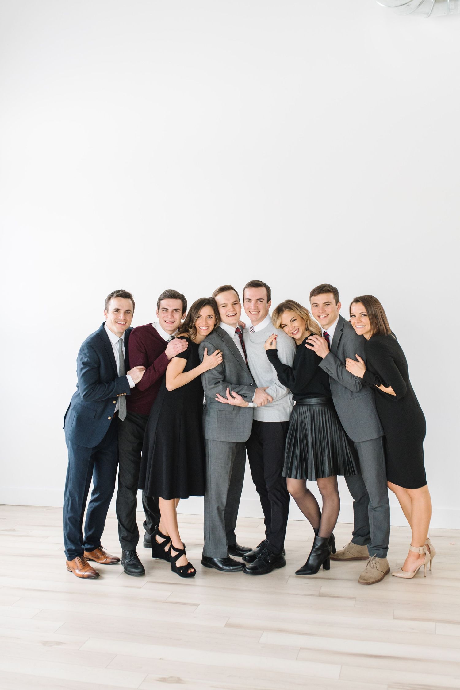 Group portrait of ten people in formal attire posing playfully together against a white studio backdrop.