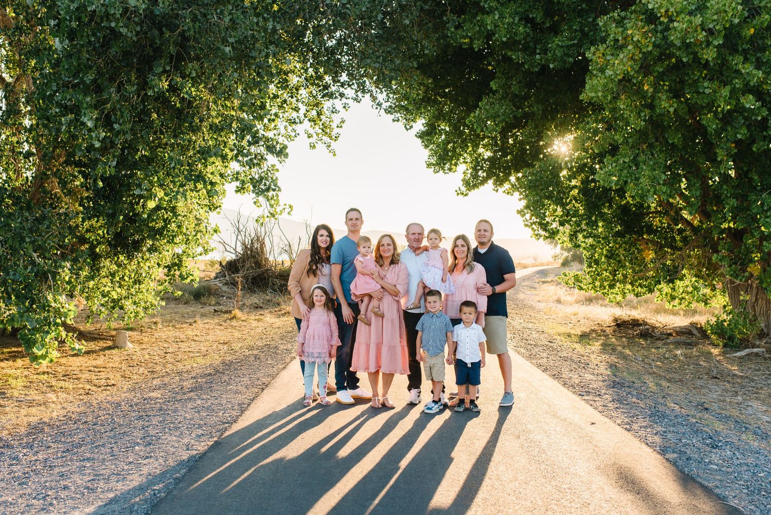 Group portrait walking together on a sunlit dirt path framed by green tree branches overhead.