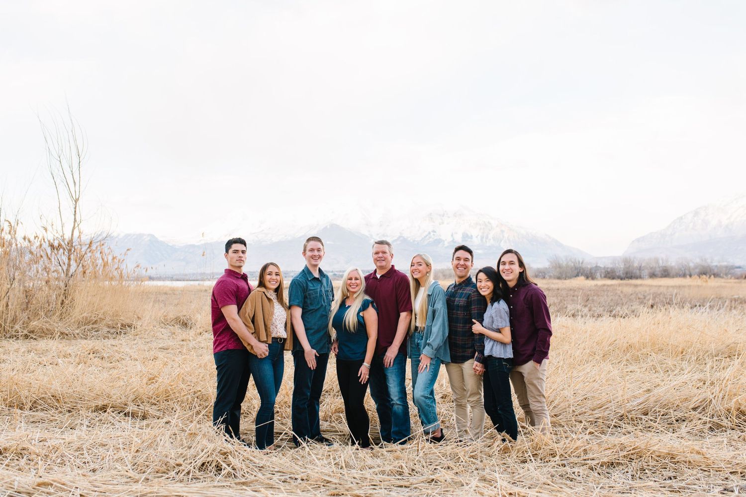 Group portrait of family members in casual attire against winter mountain landscape.