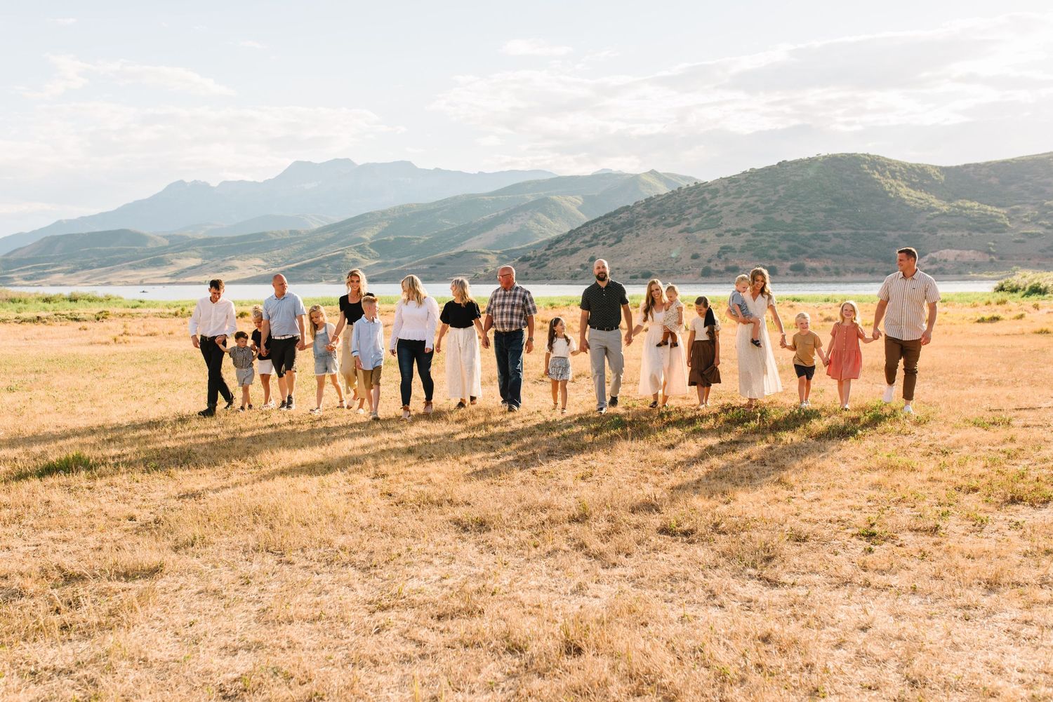Large group walking together across golden field with mountains in background.