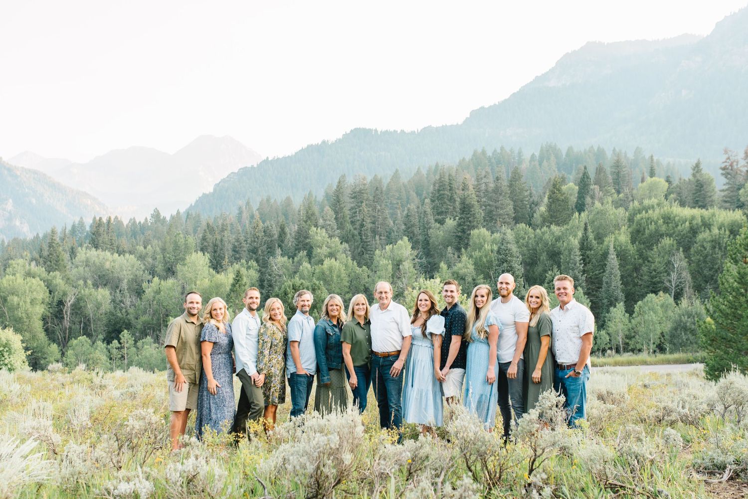 Family portrait in mountain meadow with evergreen forest backdrop.