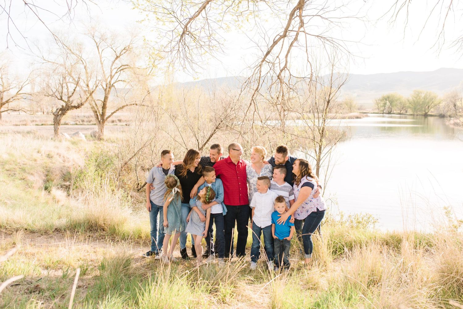 Multi-generational group gathered near a serene lake during autumn with bare trees in background.