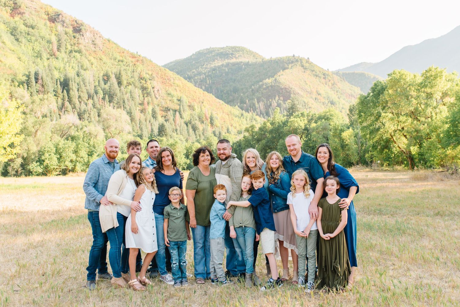 Large group portrait in casual attire against a scenic mountain backdrop with green foliage.