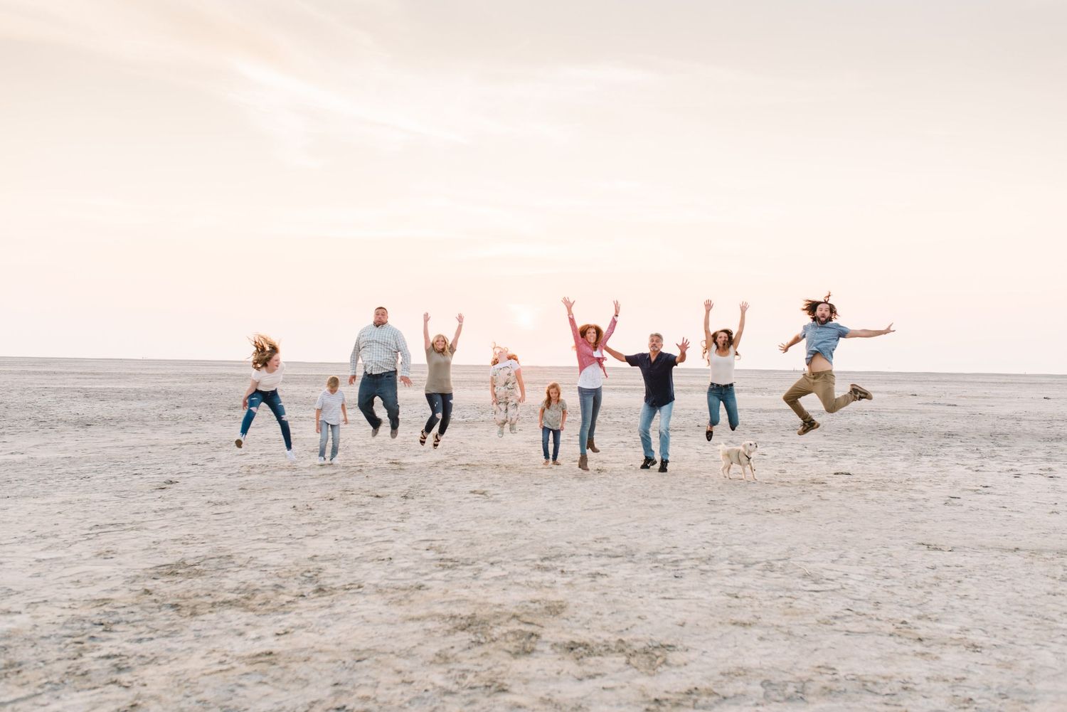 Group of people jumping together on salt flats at sunset.