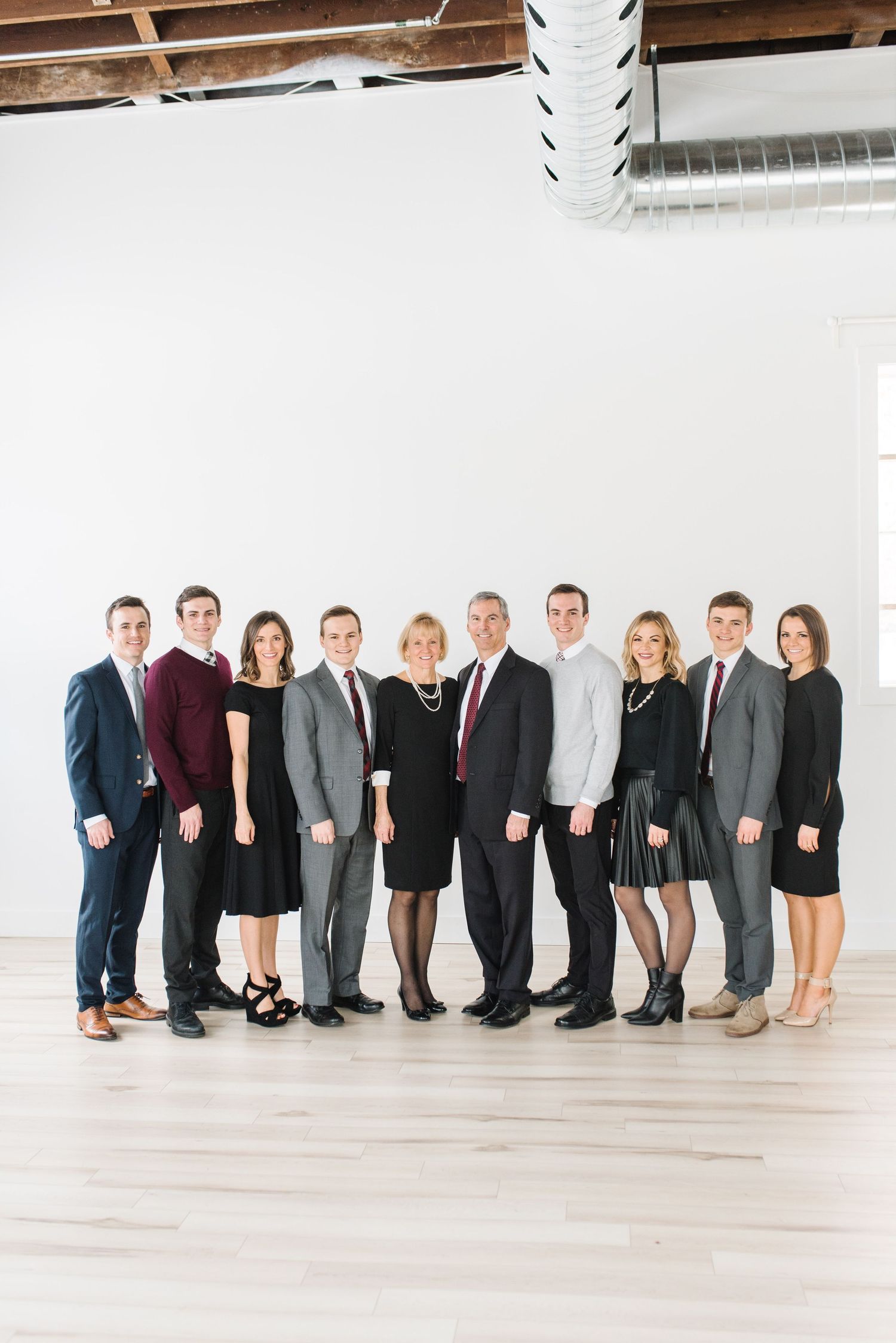 Professional group photo of ten people in formal business attire standing together in a bright white studio setting.