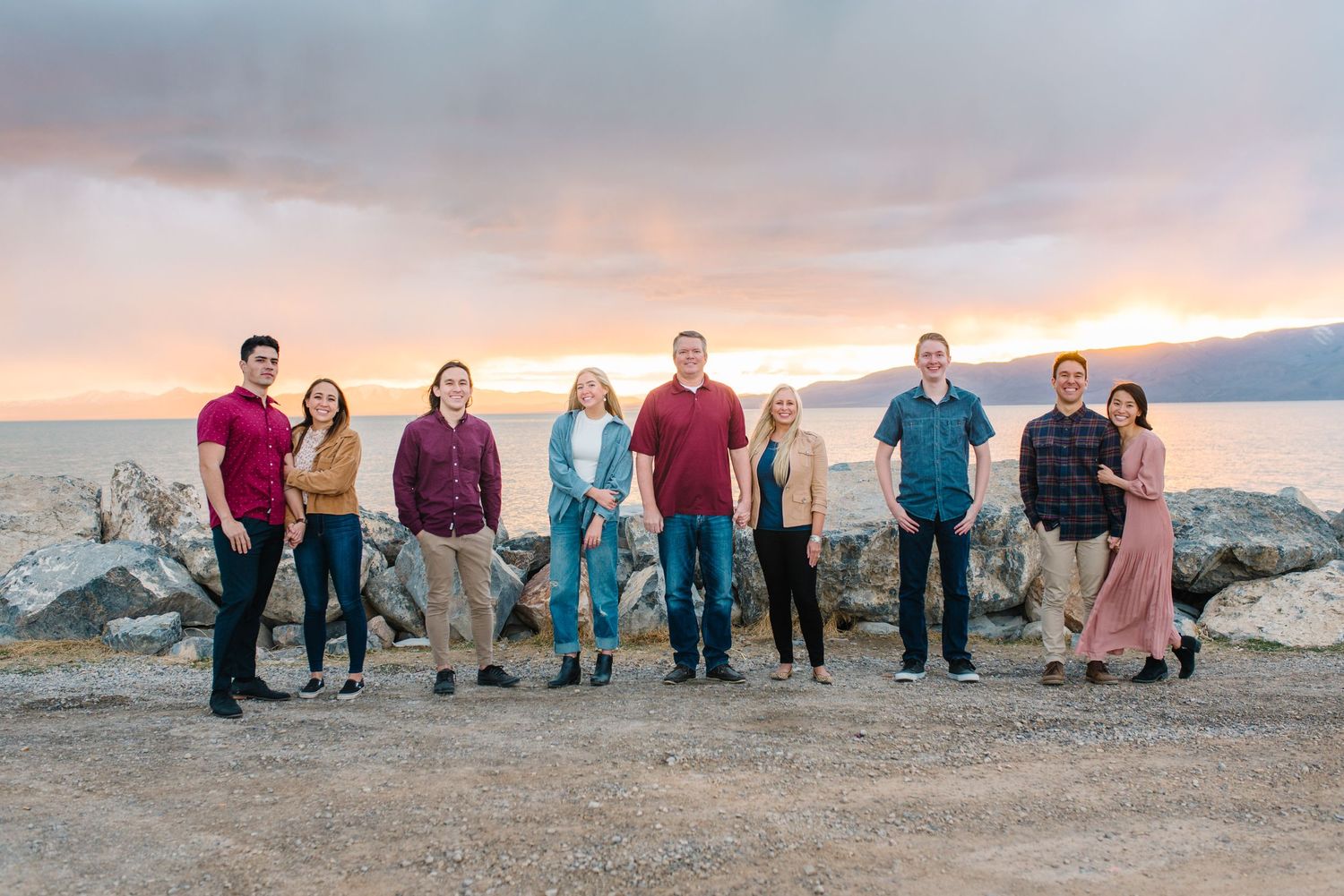 Group photo of people standing together on rocky beach during sunset with colorful sky in background.