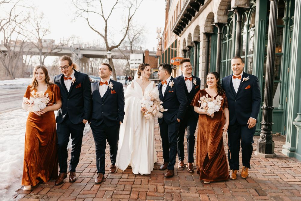 Bridal party strolls on urban brick walkway in coordinated rust and navy outfits.