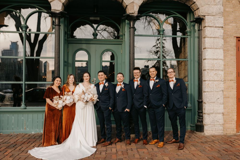 Wedding party poses outside historic building with green doors in navy and burnt orange.