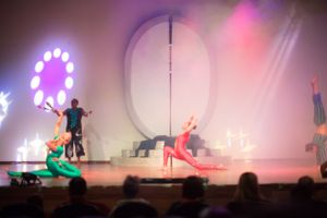 Performers on stage create dynamic movements under colorful theatrical lighting during a dance show.