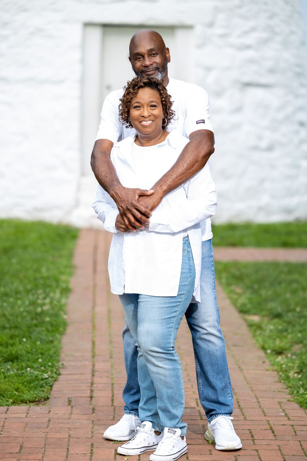 Heartwarming embrace between two people in white shirts against white lighthouse wall.