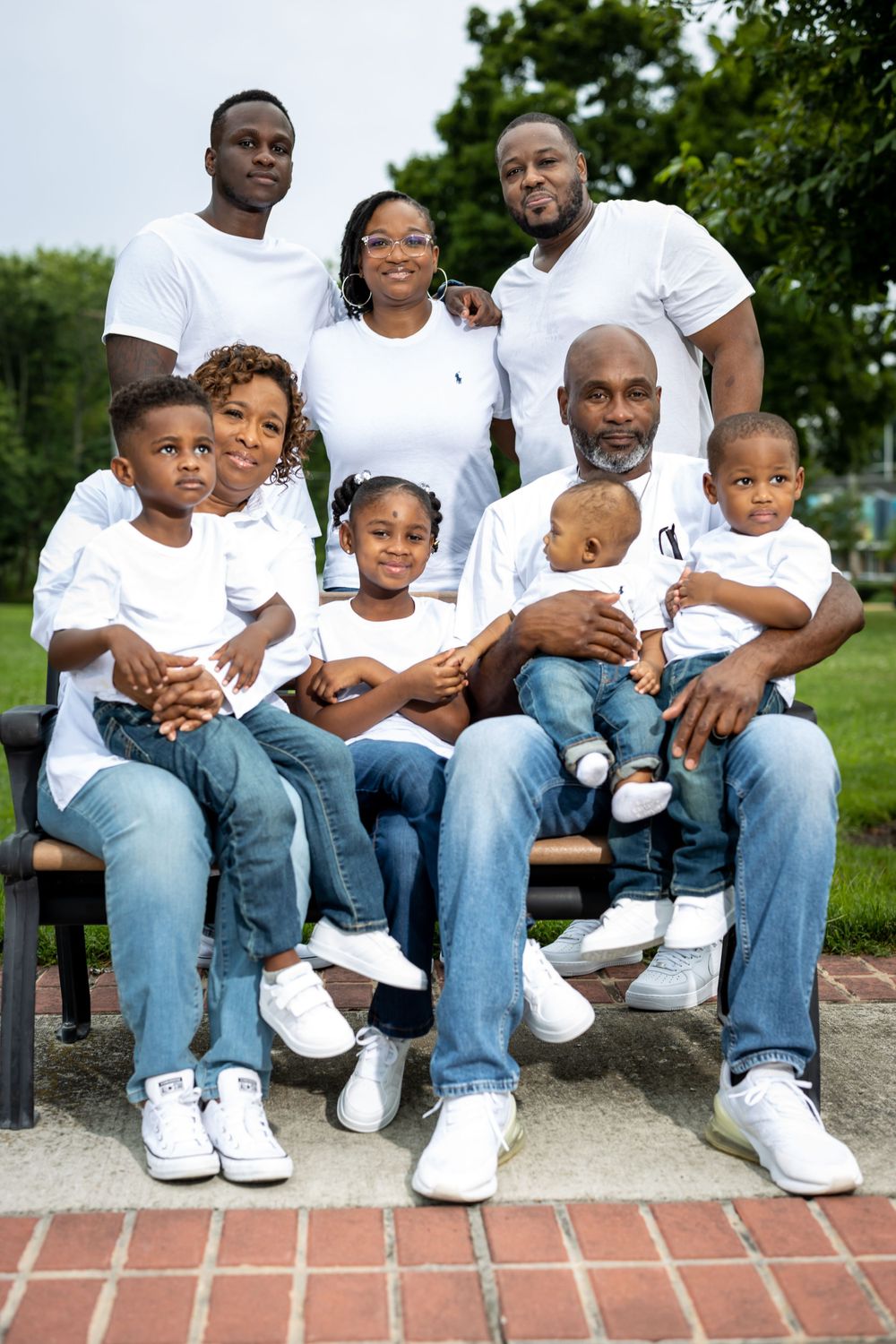Family wearing coordinated white shirts and jeans poses together on outdoor bench for portrait.