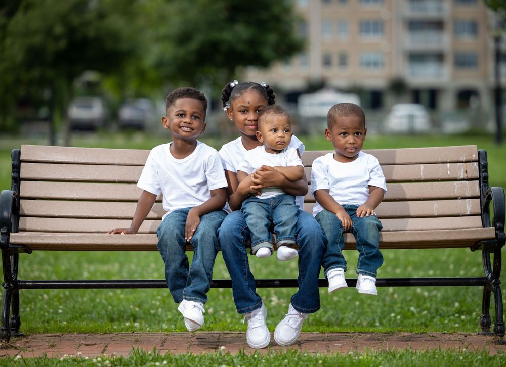 Young children sit together on wooden park bench wearing matching white shirts and jeans.