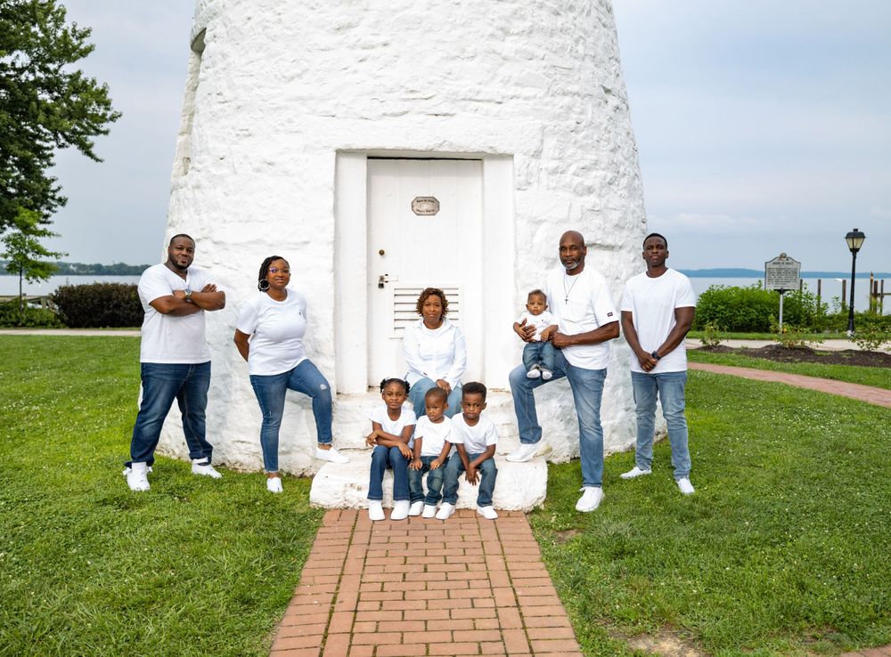 Family members in matching white shirts gather for portrait in front of historic white lighthouse.