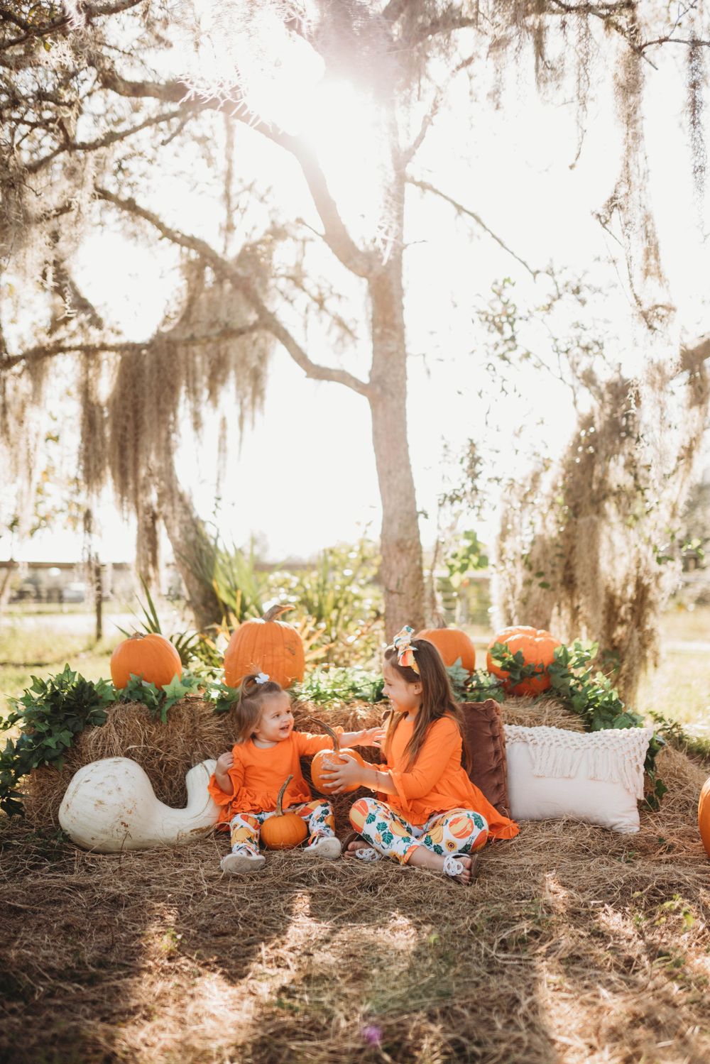 Fall themed outdoor photo setup with pumpkins and hay bales under Spanish moss draped trees.