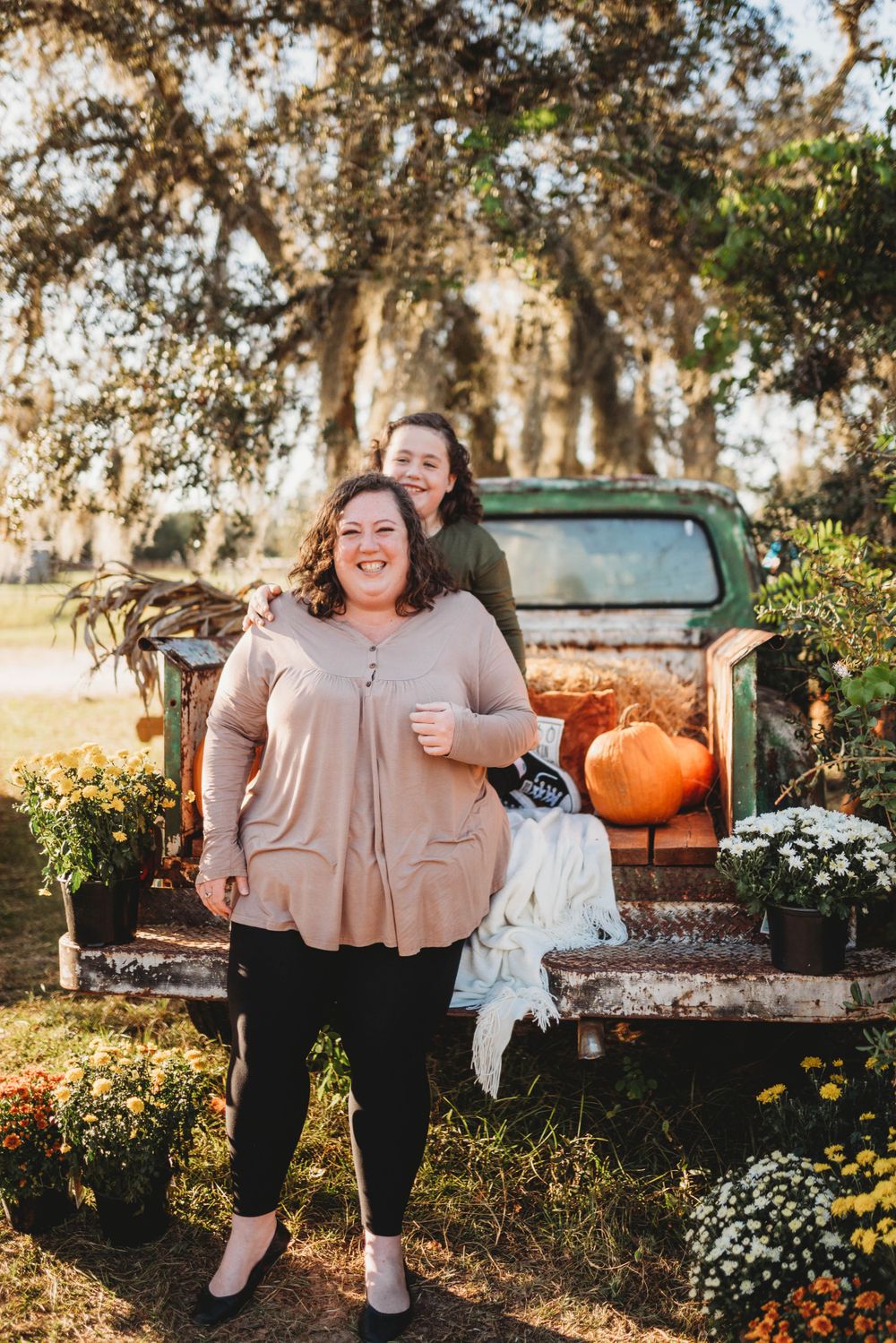 Two people pose in front of vintage truck decorated with pumpkins and flowers for autumn photos.