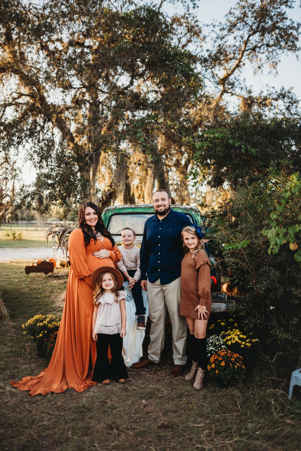 A fall family portrait with pumpkins under oak trees at sunset.