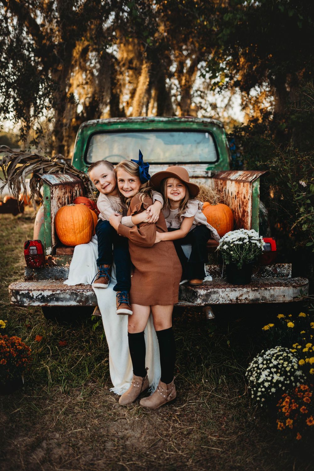 Children hugging and laughing on a vintage truck bed decorated with fall pumpkins.