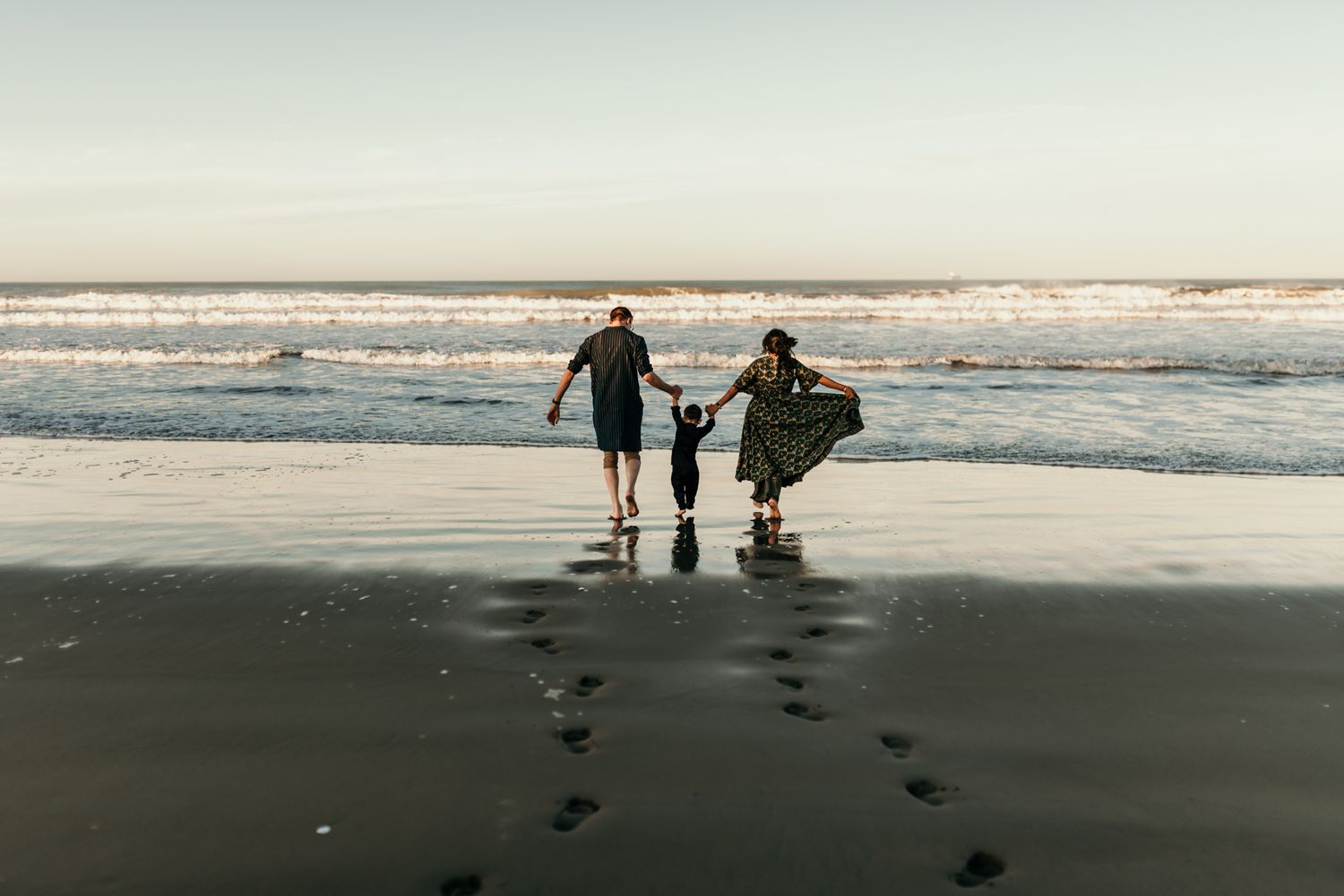 Two figures walking along beach leaving footprints in wet sand at sunset.