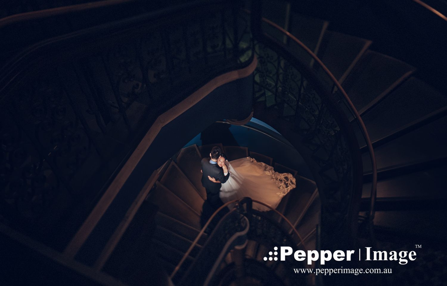 Aerial view of wedding couple sharing intimate moment on ornate spiral staircase.