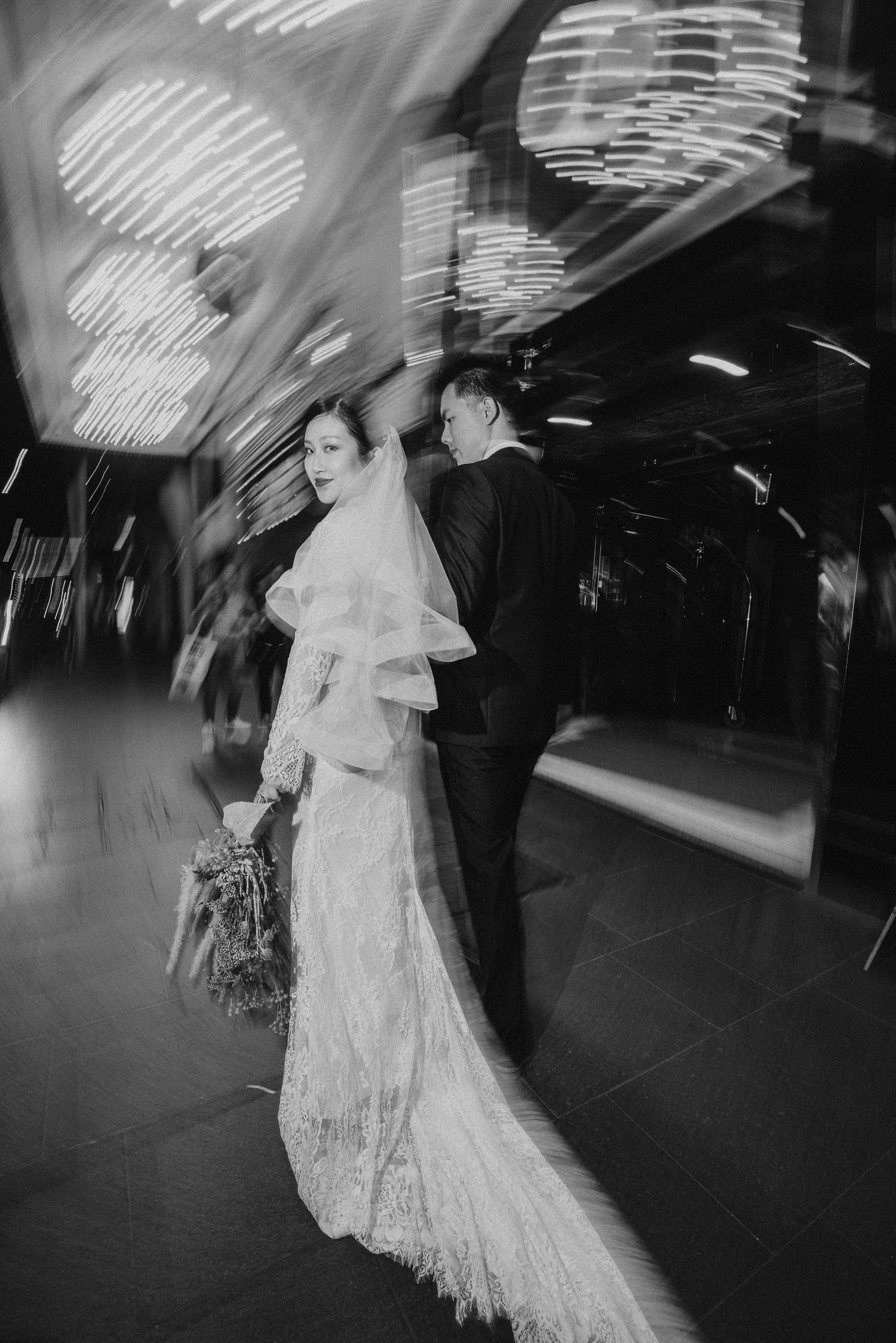 Black and white wedding portrait of bride in lace gown and groom sharing an intimate moment indoors.