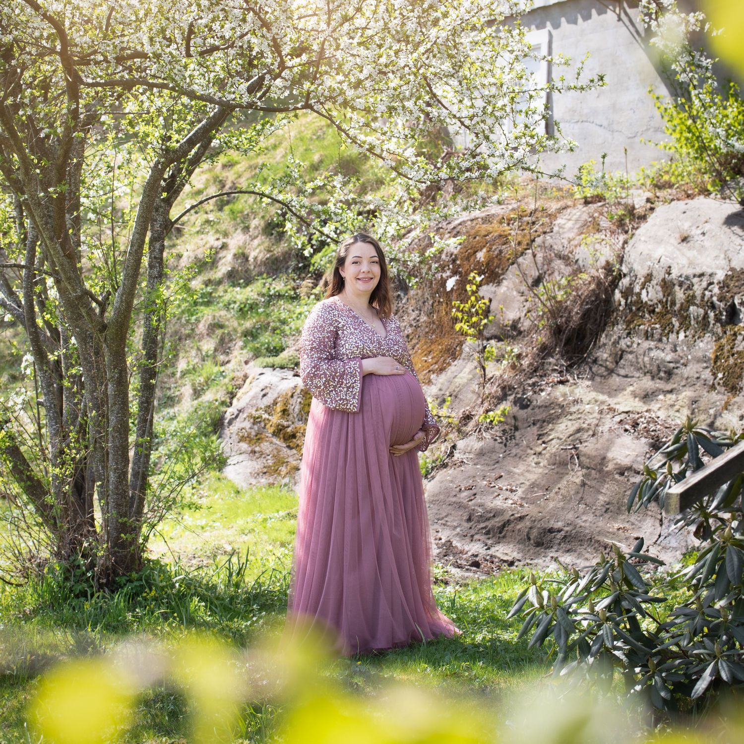 Outdoor maternity photo under blooming trees wearing mauve tulle dress.