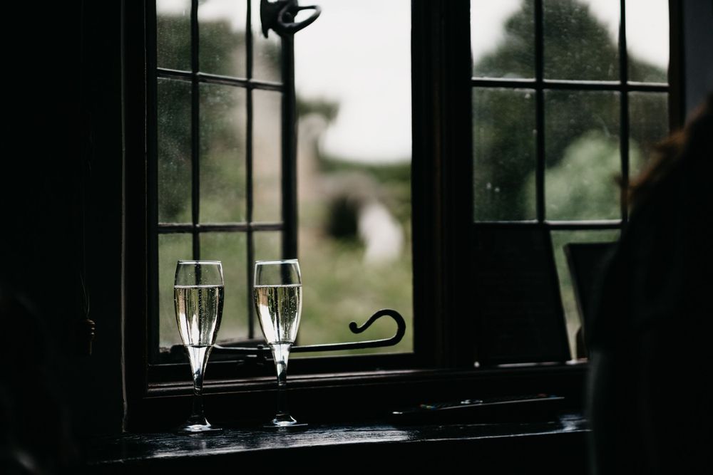 Two champagne glasses sit on a dark windowsill overlooking a blurred outdoor landscape.