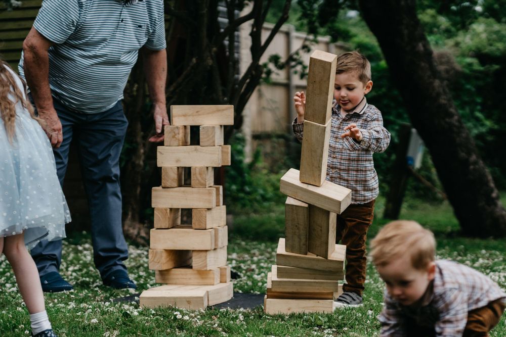 Children playing with a large wooden block stacking game in a garden setting.