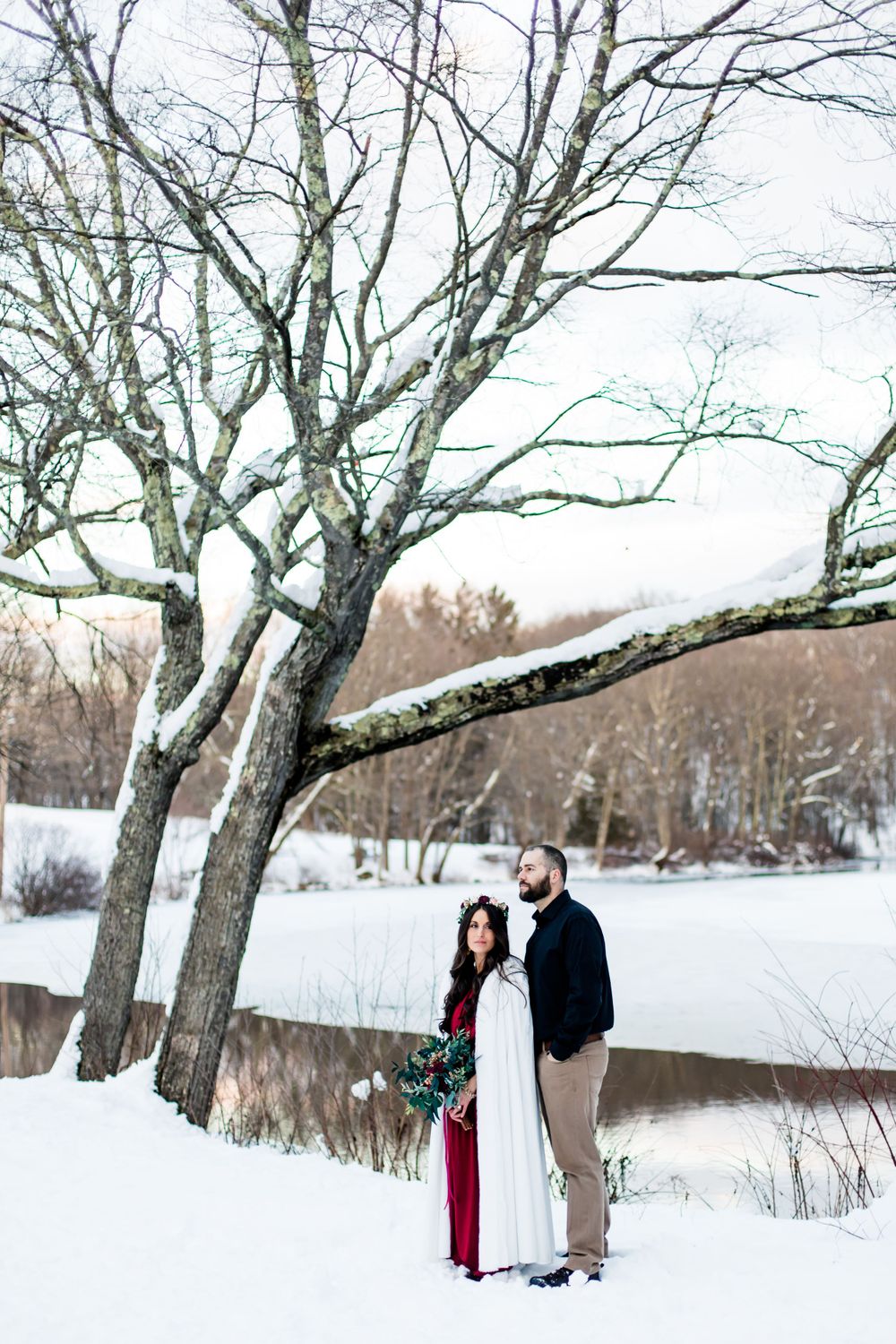 Scenic winter engagement photos under bare branches with snow-covered ground.