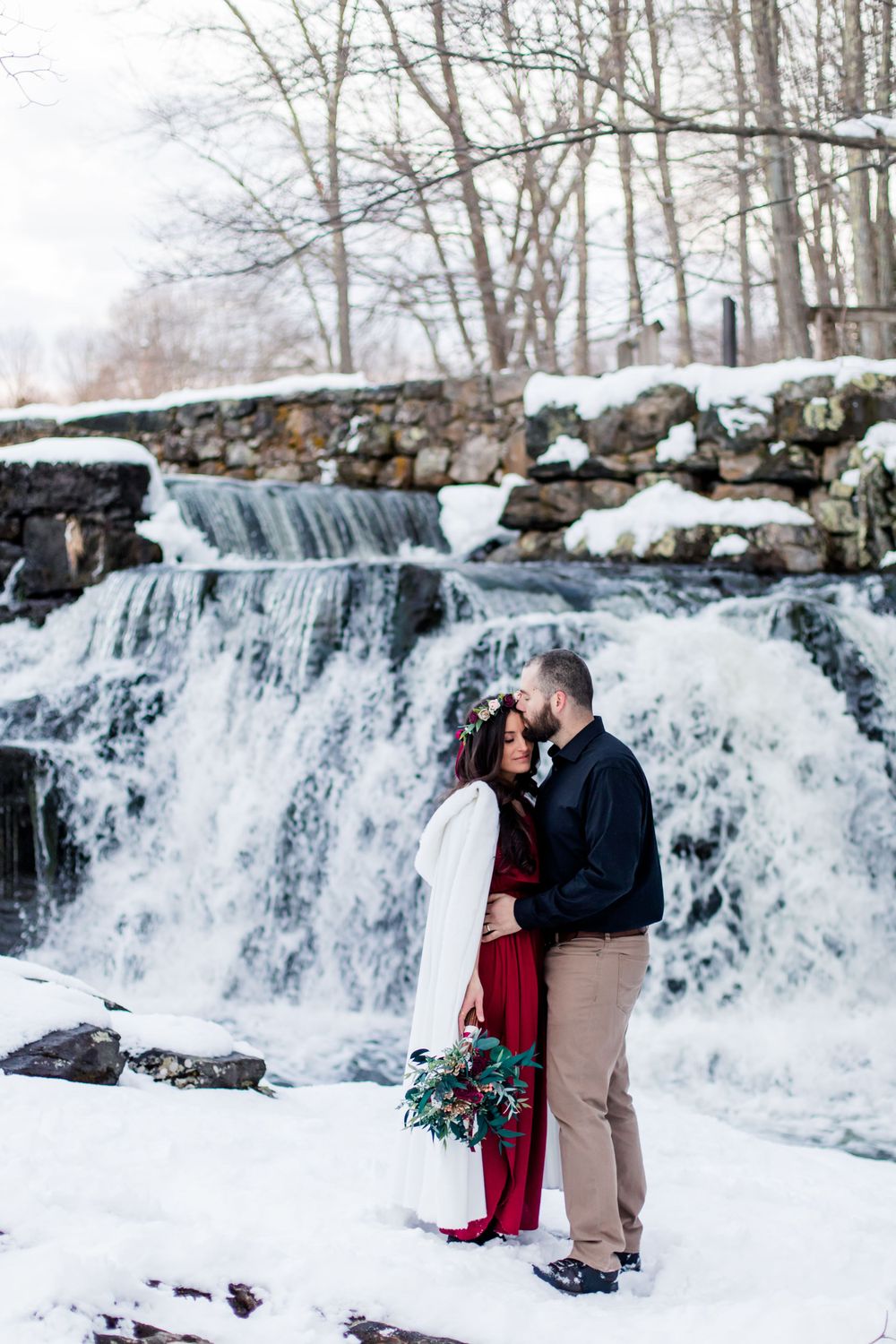 Couple poses in front of frozen waterfall during winter engagement session.