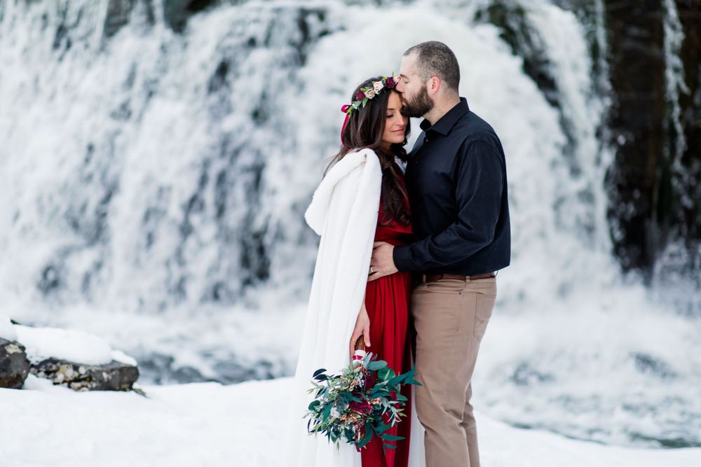 Romantic couple embraces by snow-covered waterfall in winter setting.