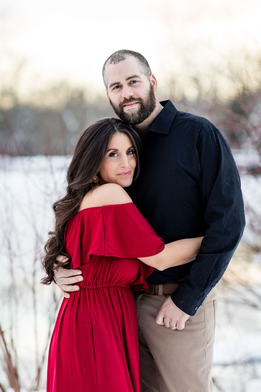 A winter portrait of a couple embracing, with the woman wearing a red dress in the snow.