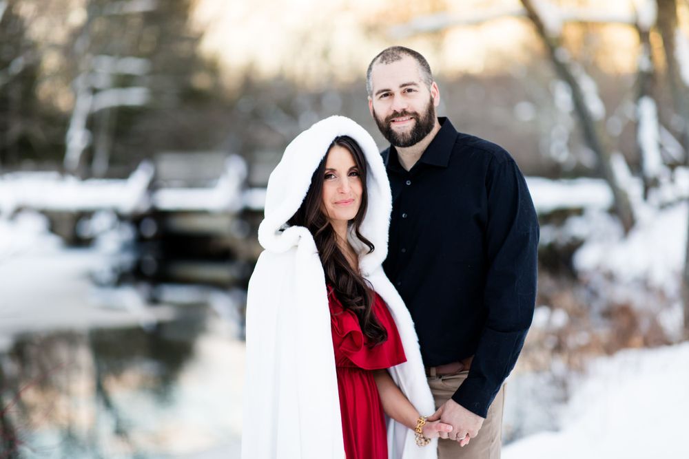 Romantic winter engagement photos in a snowy landscape with couple in red and black attire.