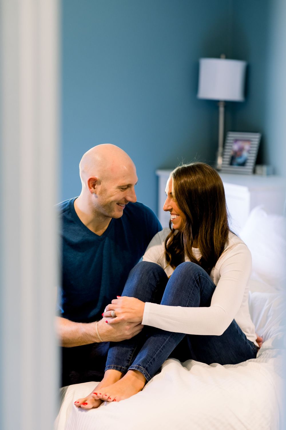 A candid moment between a couple sitting on a white bed against a blue wall.