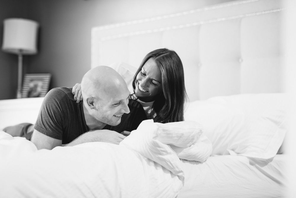 A black and white intimate photo of a couple sharing a playful moment on a bed.