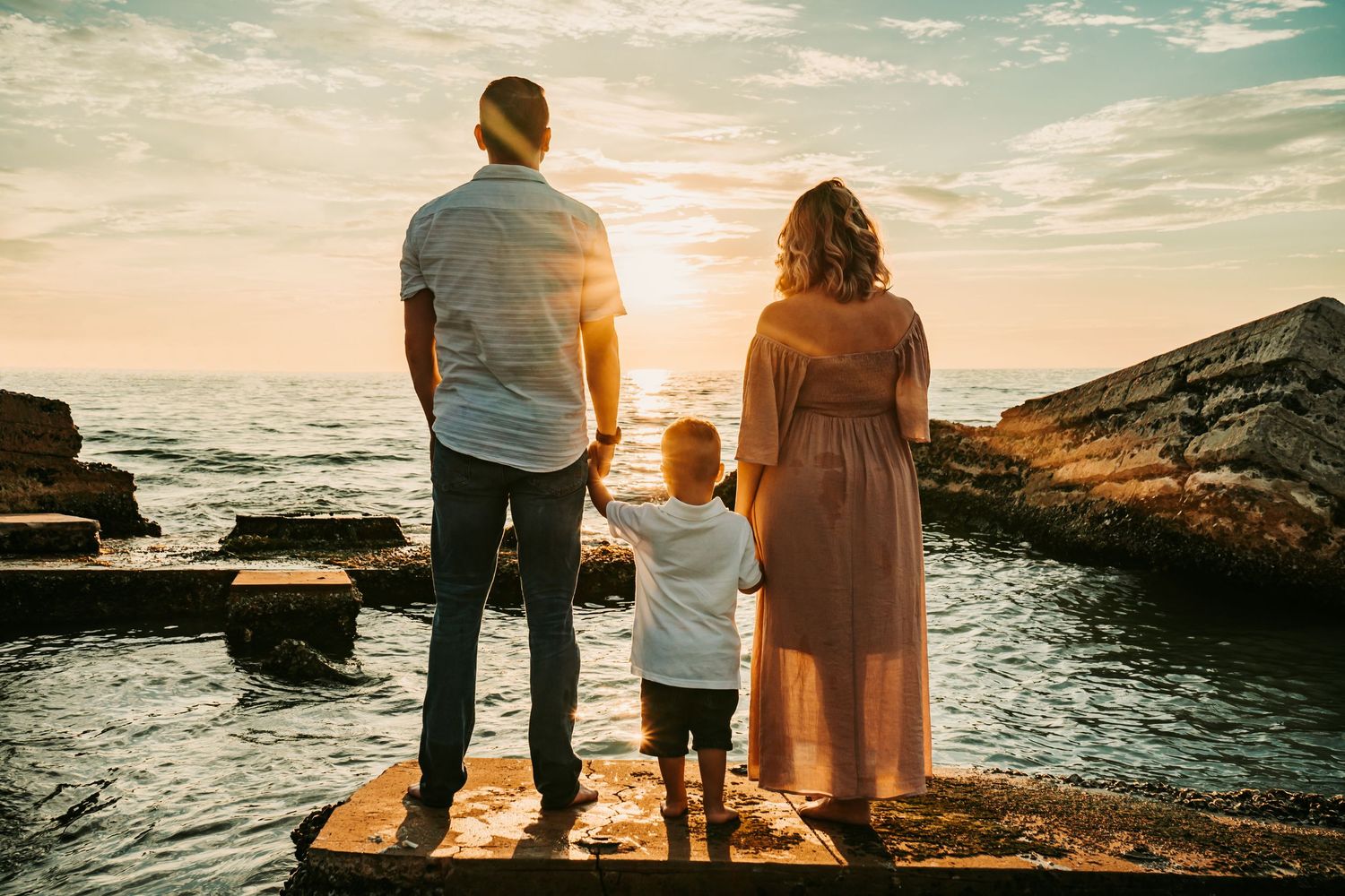 Outdoor Maternity Session at Ft. Desoto in St. Pete, FL; Family faces out to the sunset while standing in front of ruins on a beach