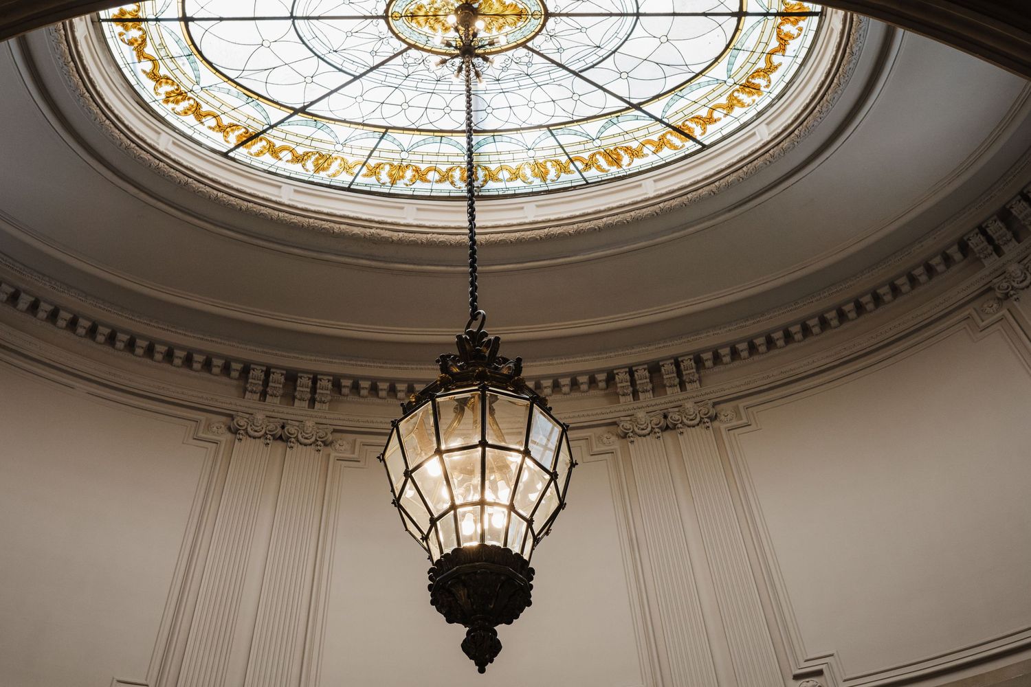 Elegant stained glass dome ceiling with hanging vintage lantern in a classical interior.