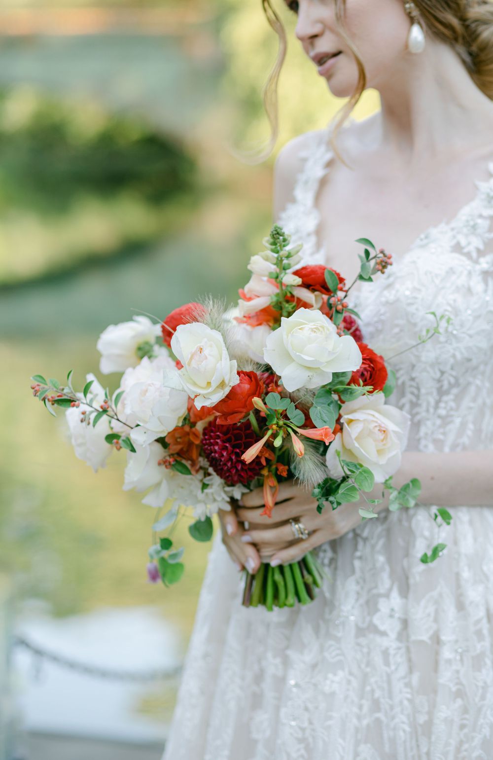 White and red wedding bouquet with roses held against lace wedding dress.