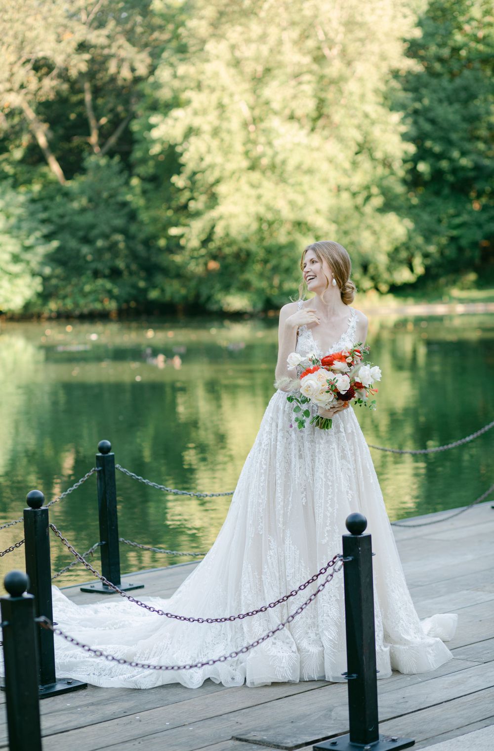 Wedding dress silhouette on wooden bridge over pond with floral bouquet.