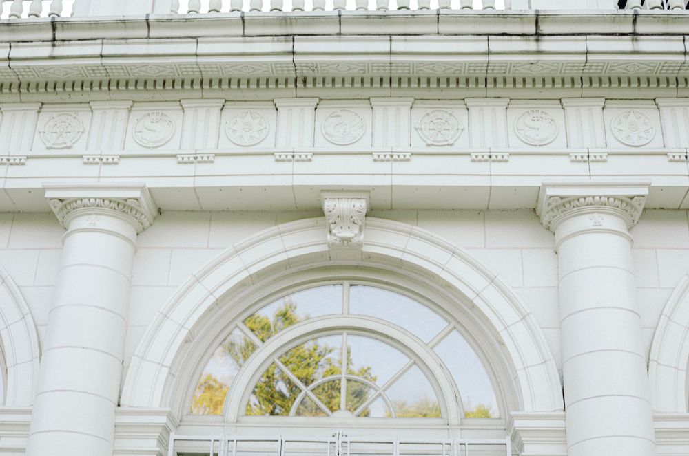 Classical architectural detail of white columns and arched window with ornate trim.