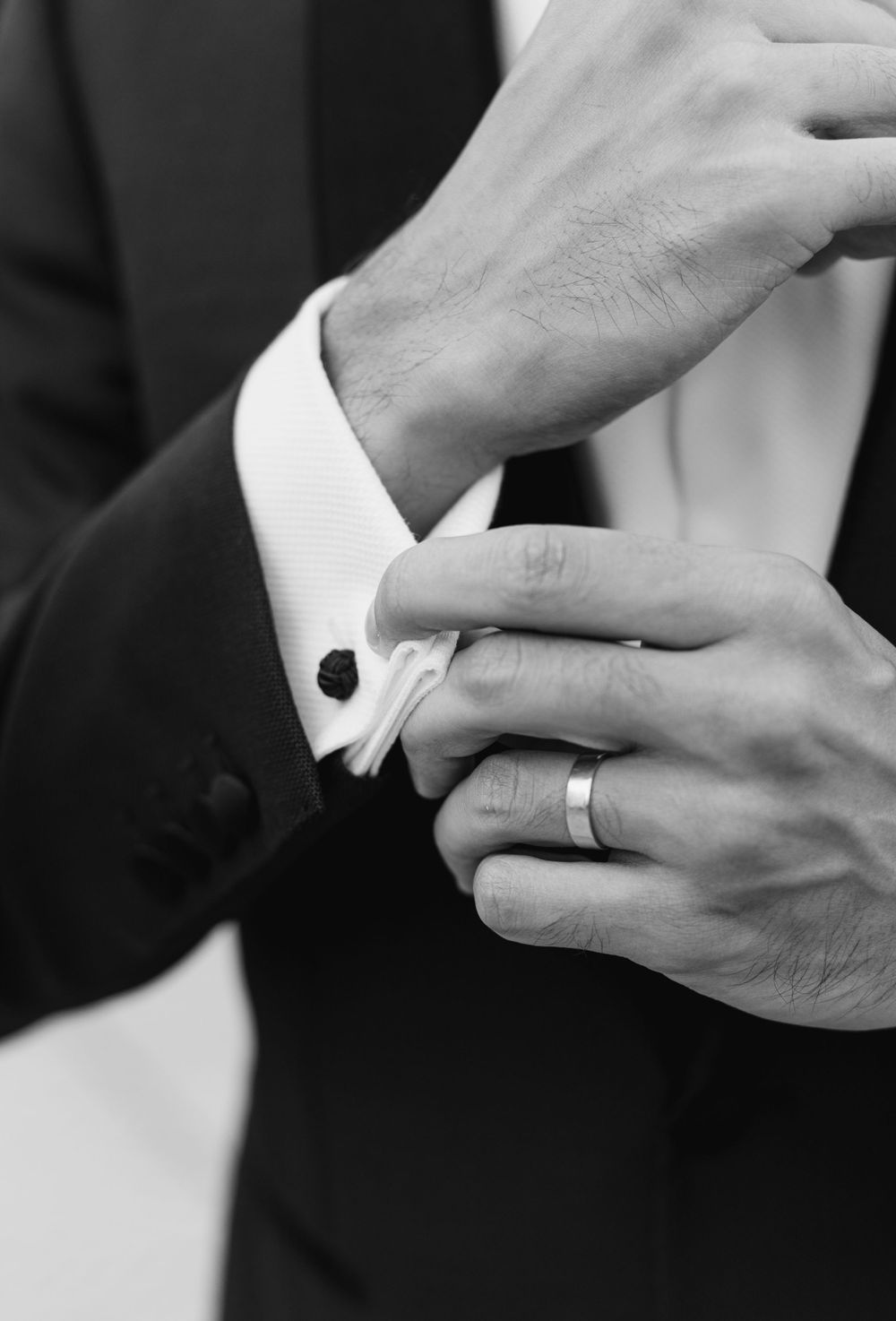 Close-up of hands adjusting a white shirt cuff with cufflinks and wedding ring.