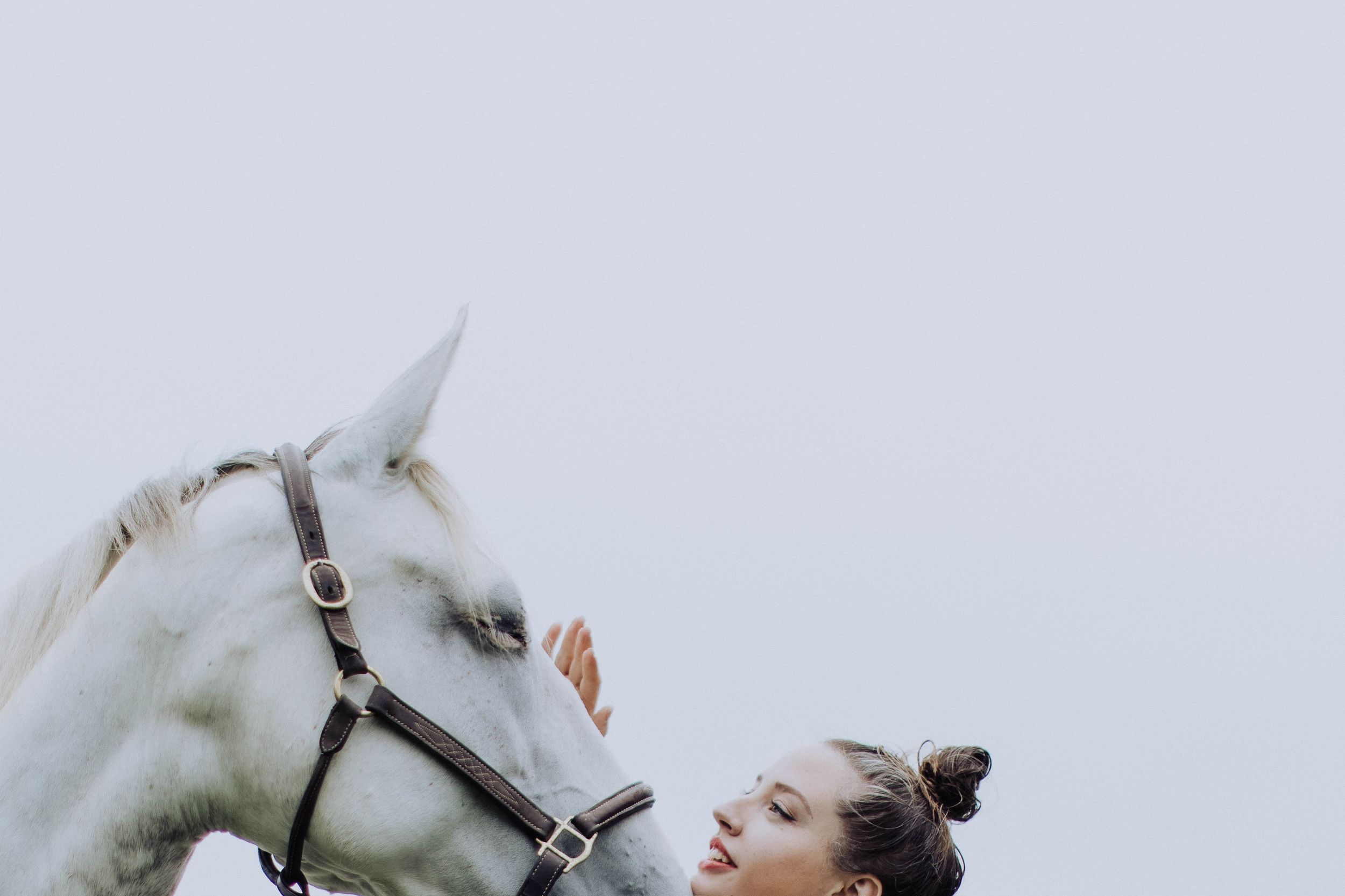 Ethereal outdoor portrait with white horse against light background.